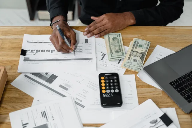 Man working on financial reports with calculator, money, and laptop on a desk. A blank budget template for hiring a branding agency, VAT field included